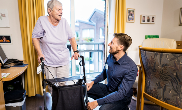 Mann kniet neben älterer Dame am Rollator